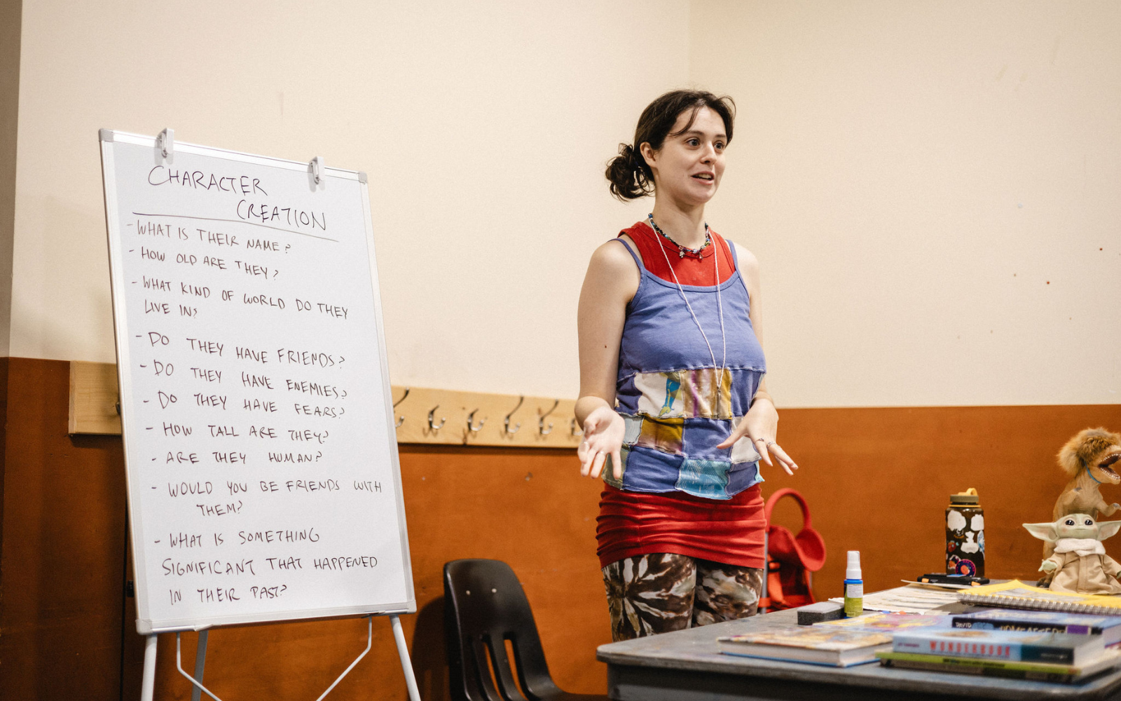 A workshop facilitator standing and talking at the front of a classroom next to a whiteboard that says "Character Creation."