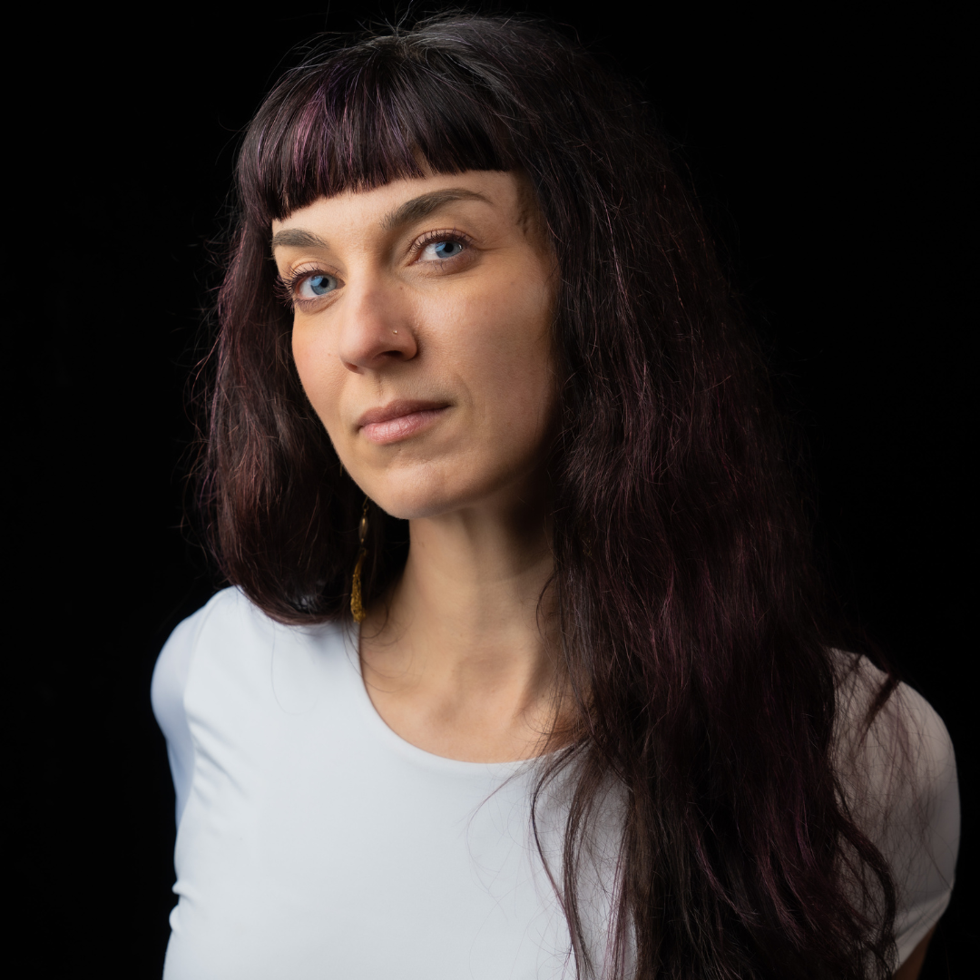 A portrait of woman in front of a black background with long dark hair and short bangs. 