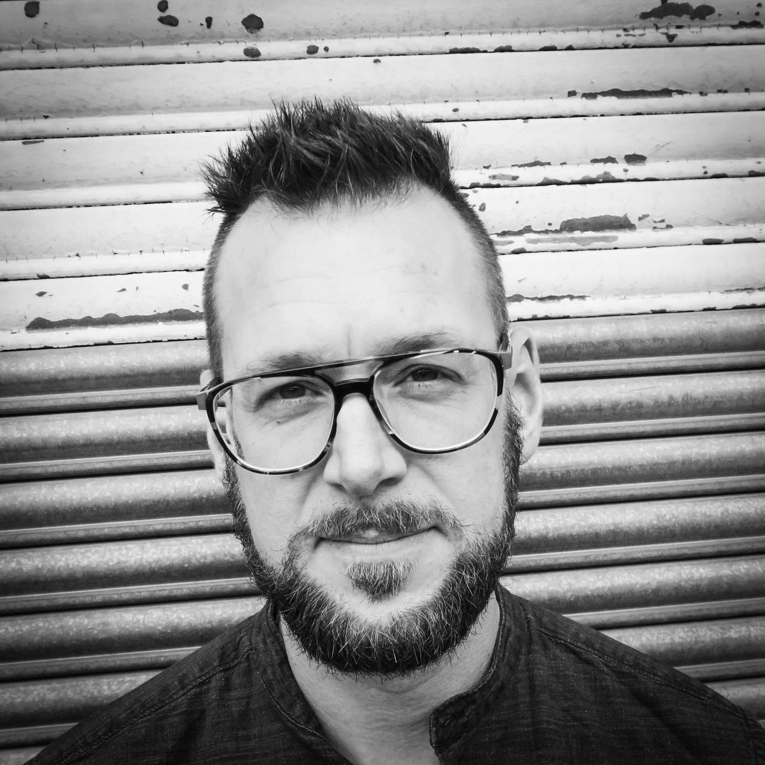 Black and white portrait of a man with short hair and a full beard. He's wearing acetate aviator glasses.