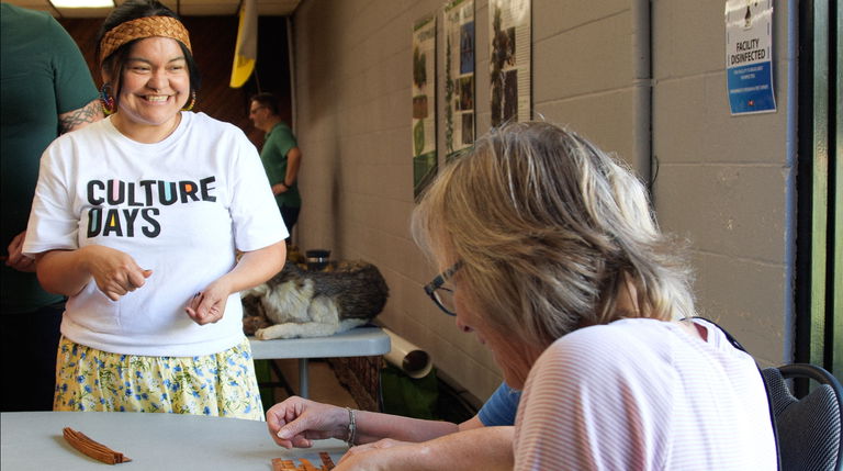 Film still from Weaving Our Story Towards Reconciliation. Priscilla connects with community members at Kinsmen Hall in Port Coquitlam and teaches them how to weave cedar hearts.