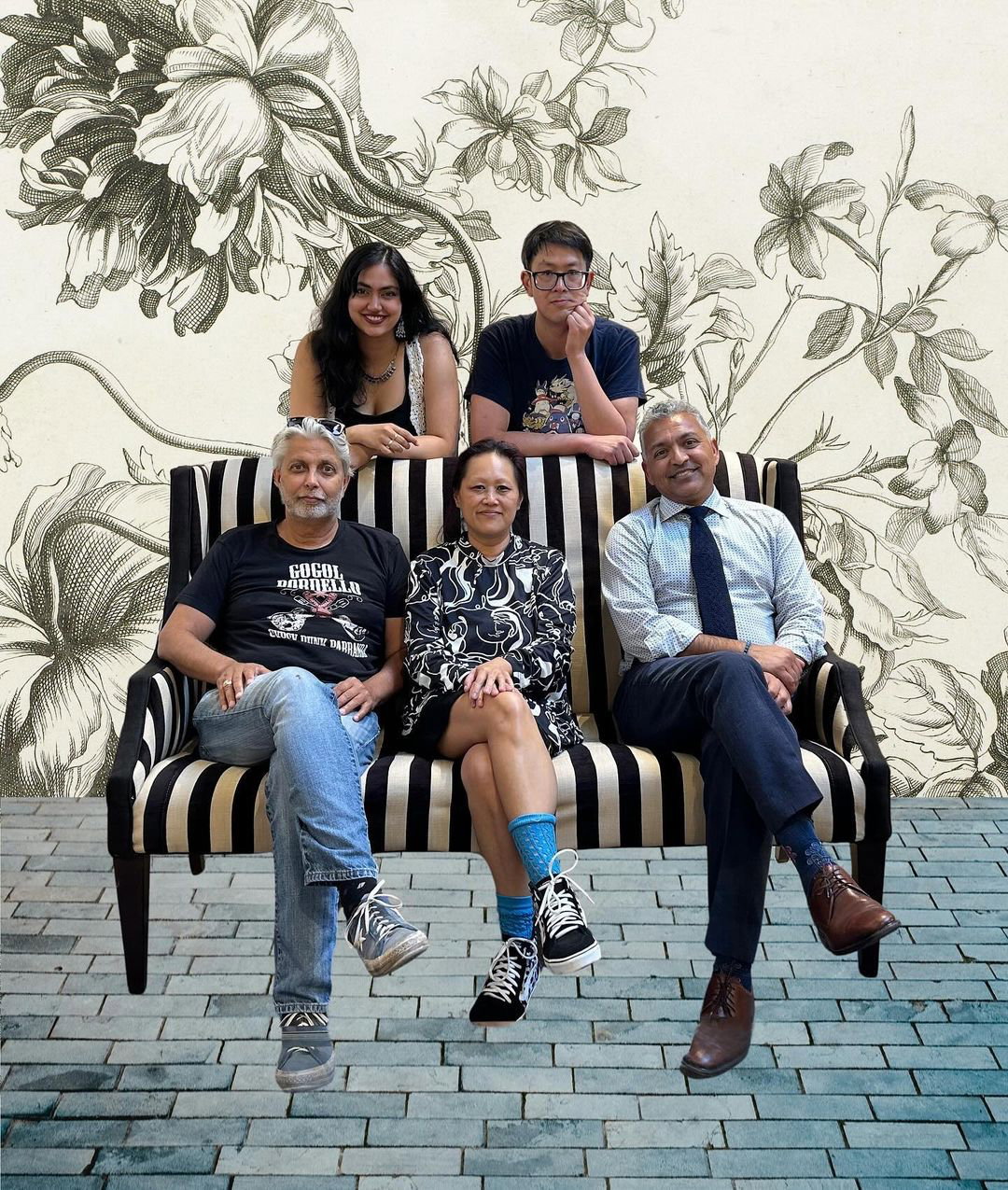 Five people sitting on and leaning on a striped couch posed for a portrait where they are all smiling. 