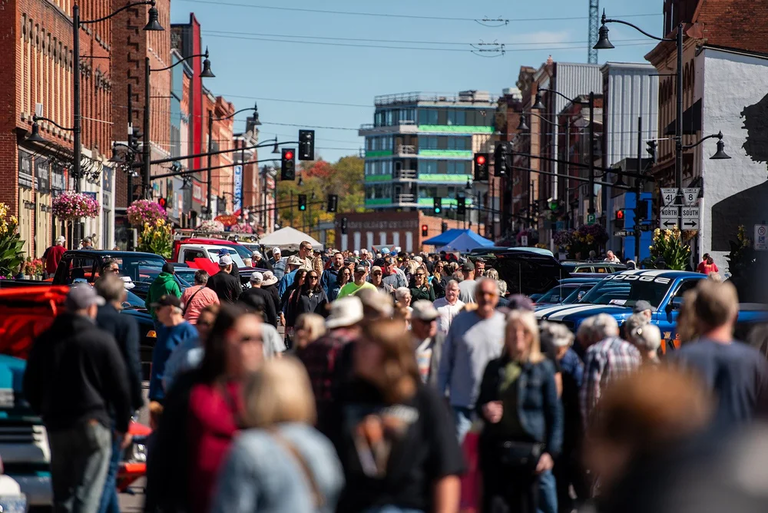 crowd of people in a busy downtown looking at old cars.