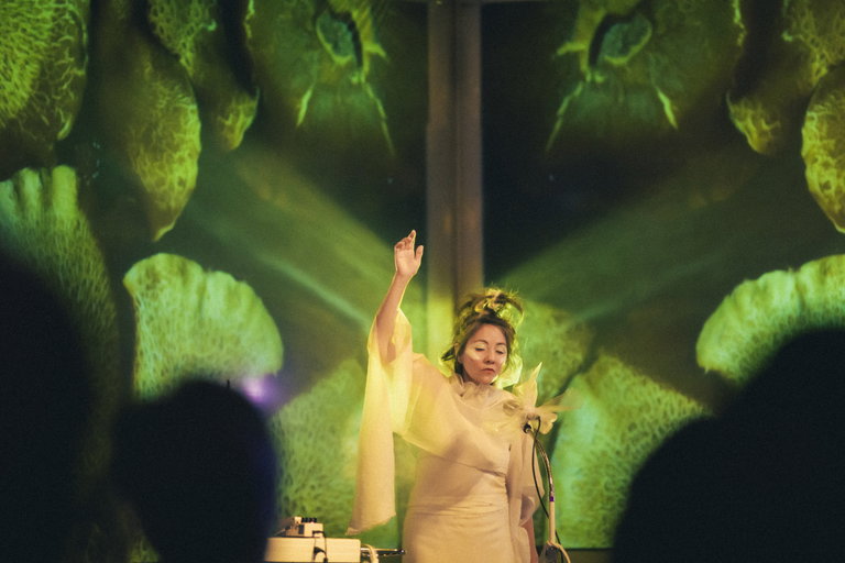 óFukami performing on stage at Cluster Festival, with Joel Penner's projected visuals glowing behind her.