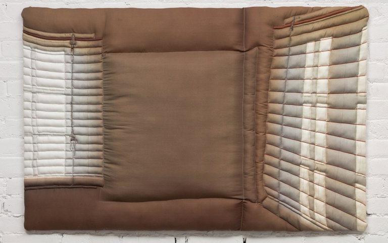 Photograph of Childhood Home by Maya Beaudry, hanging on a white brick wall. The artwork depicts a corner of a room, with large windows with closed blinds on the left and right.