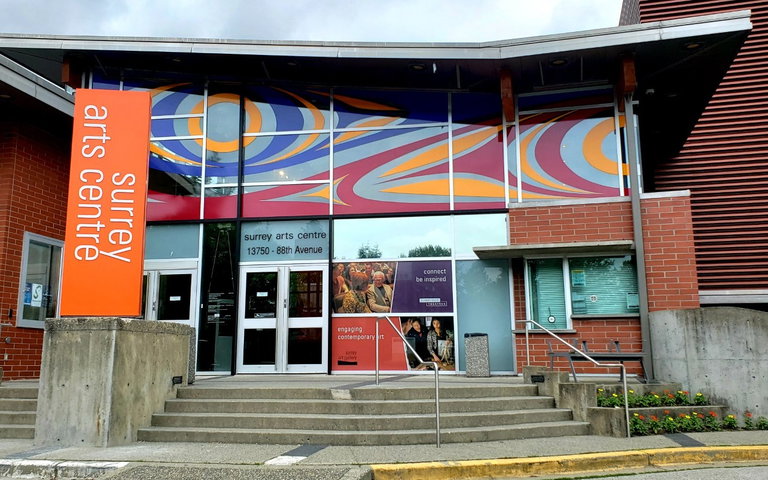 An abstract vinyl mural of blues, reds, and yellows in circles, trigons, and ovals spans the top windows of the entrance to Surrey Arts Centre.