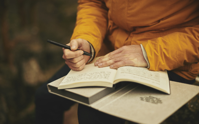 A person in an orange jacket writing in a journal