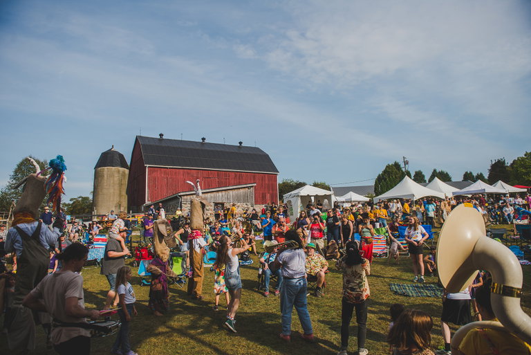 Festival guests gather on the lawn at Haute Goat Farm while a brass band and stilt walkers parade through the crowd in front of the iconic red barn during Cultivate Festival.