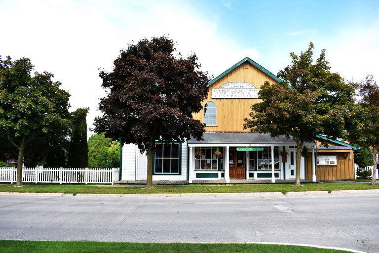 Historic museum building with a wooden façade, trees, and a white picket fence along the street.