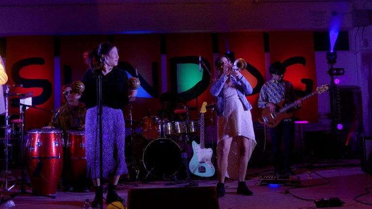 Empanadas Illegales play at the Sundog Festival. The are on a stage with large colourful Sundog Festival letters behind them.