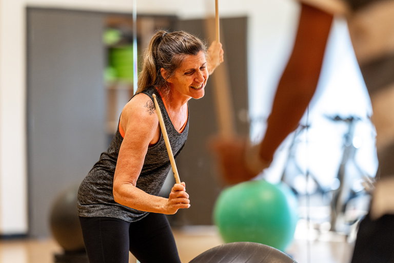 An instructor in the fitness studio using drumsticks on an exercise ball.