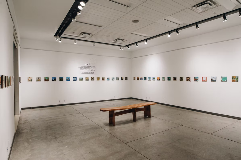 Photo of gallery space with small uniform artworks lining the perimeter.