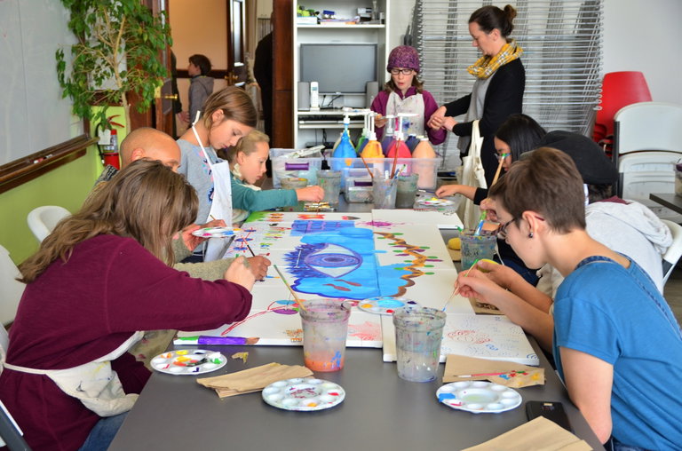 a Group of youth and adults around a table, taking part in a collective painting.