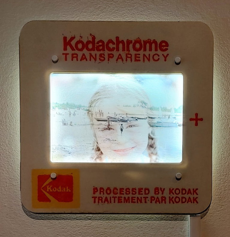 an old fashioned slide blown up large that depicts a young girl's face layered on top of a busy beach.