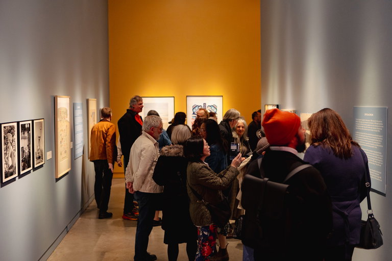 Crowd of people viewing artwork hanging in a gallery.