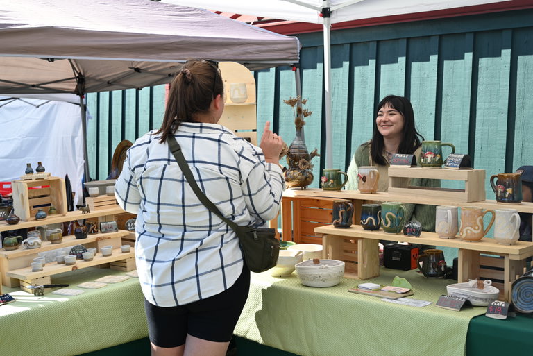 A vendor selling their handmade pottery and smiling at a customer