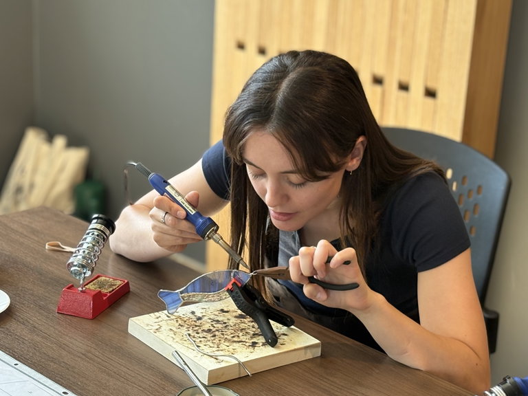Woman using a soldering iron and pliers to make stained glass fish