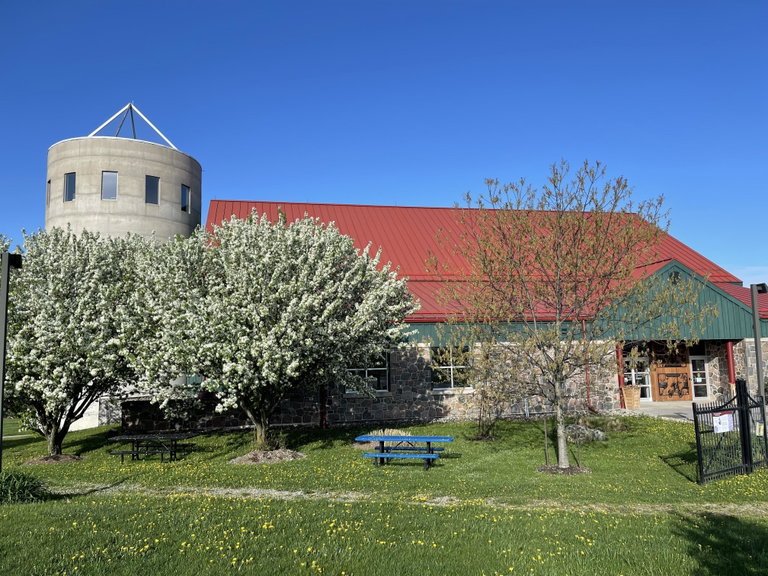 Exterior photo of a large barn with a red roof and green siding with a silo on the left