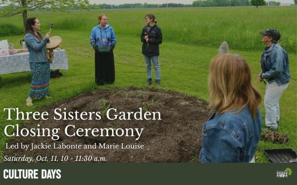 A group of women gather around a circular garden with small seedlings just planted. One woman sings and drums. They are surrounded by meadows.