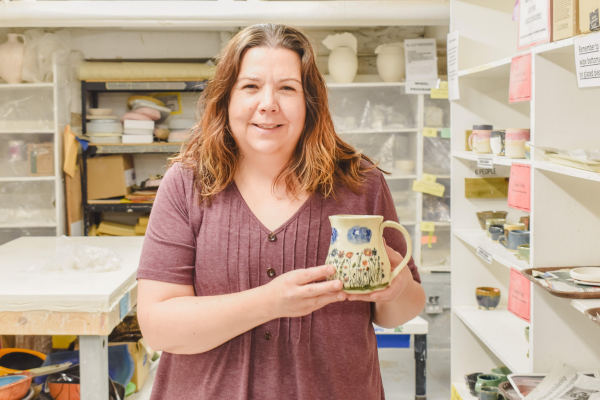 A Paint Your Own Mug participant holds up a mug for a smile