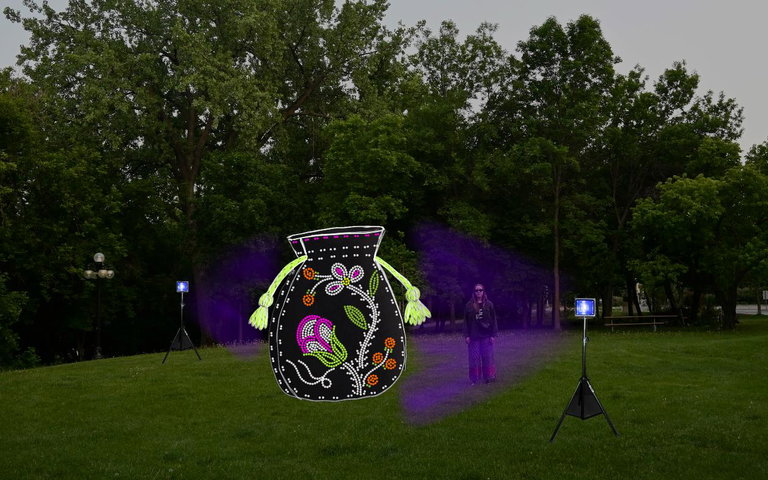woman standing in grass field with glowing medicine tobacco bag lit up by glow in the dark beads, illuminated by two standing blacklights