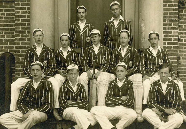An old black and white photo of the Appleby College cricket team. The group of 11 young boys are wearing striped jackets and ball caps.