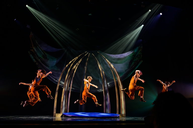 Still from Pisuwin. Dancers in work clothes in midair.