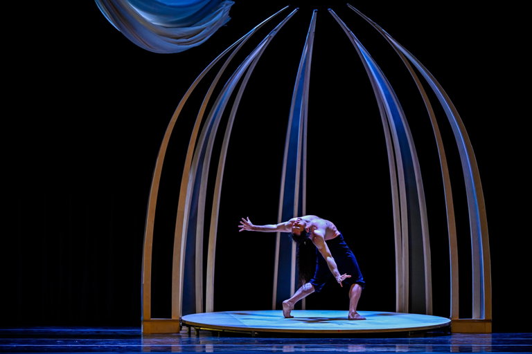 Still from Pisuwin. Dancer in a backbend under a wooden arch.