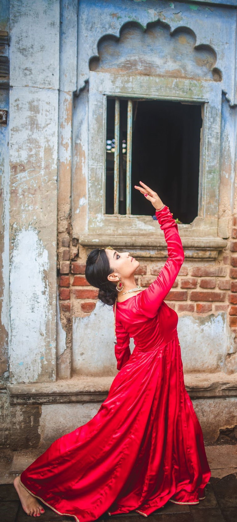 A female dancer in a red dress has her right arm raised above her head and leaning back