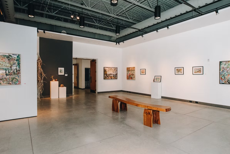 Wide shot of paintings hung in gallery.