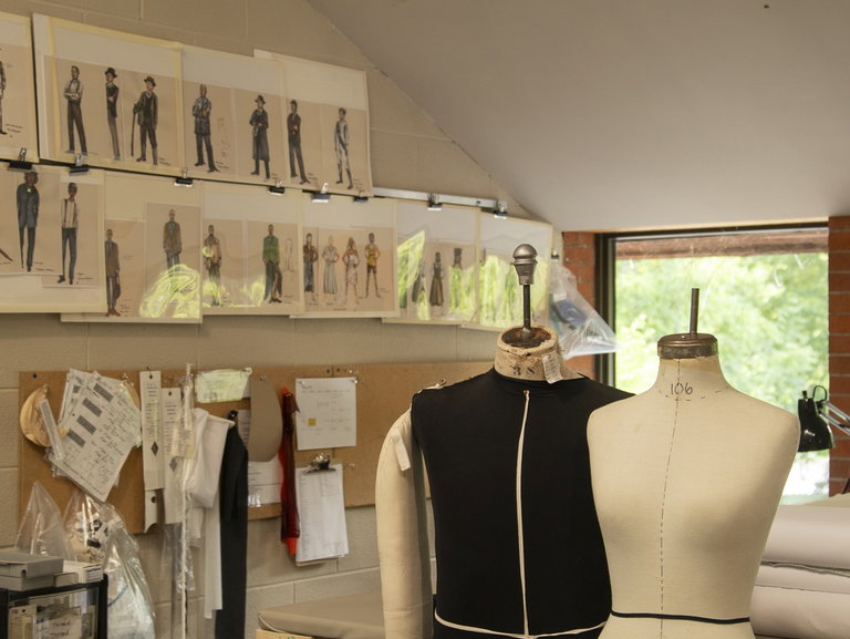 Photo of costume renderings on the wall with two dress forms without costumes.