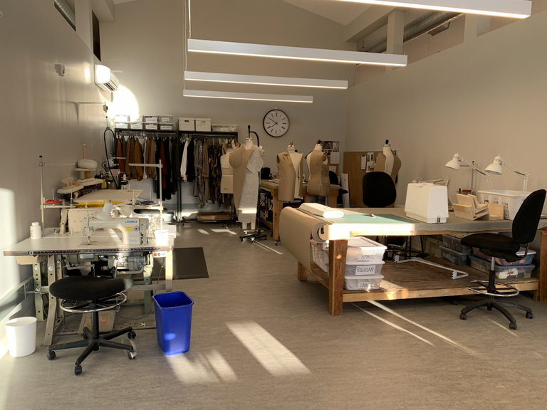 Photo of a cutting table and sewing machine with dress forms in the background.