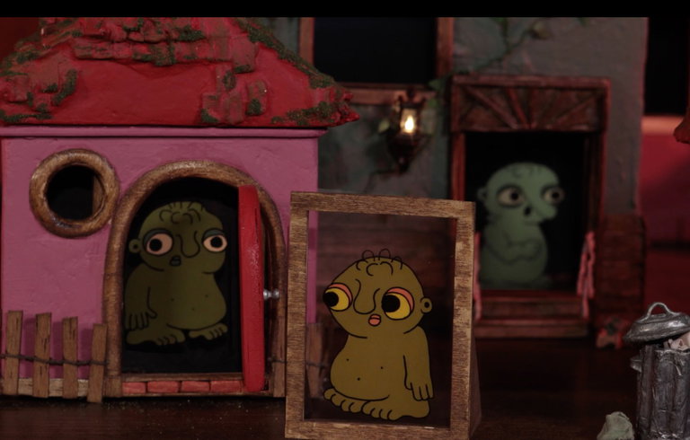 Strange moss-green creatures with large eyes inhabit doorways in a darkly colourful animated streetscape