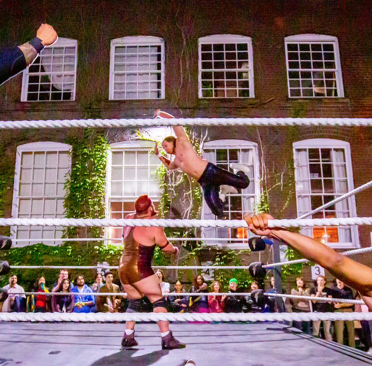 Independent pro wrestlers from Superkick’d Studios mid-match inside a pop-up wrestling ring at 401 Richmond during Nuit Blanche, surrounded by an energetic crowd in an industrial art space.
