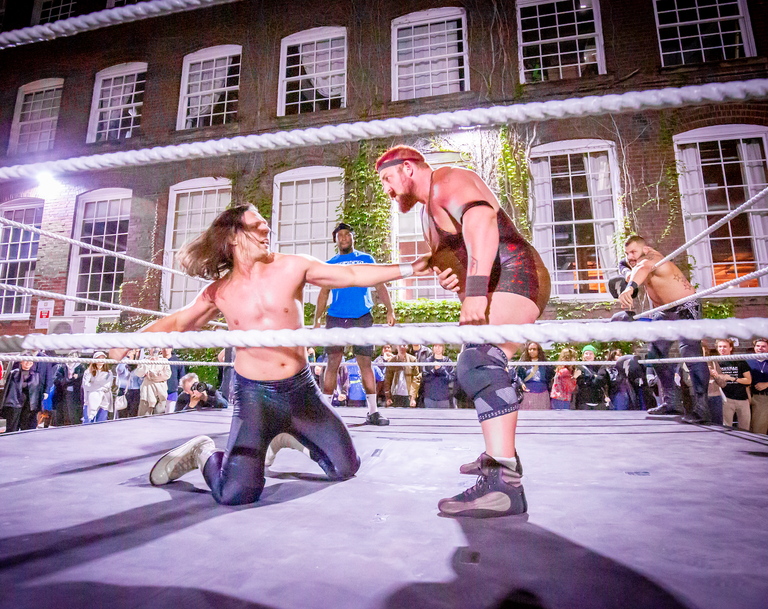 Independent pro wrestlers from Superkick’d Studios mid-match inside a pop-up wrestling ring at 401 Richmond during Nuit Blanche, surrounded by an energetic crowd in an industrial art space.