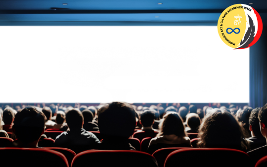 Crowded movie theatre with people sitting in red chairs facing a blank, bright white screen