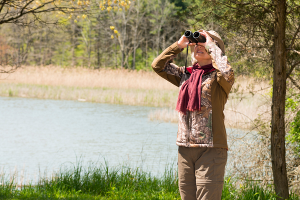 Woman standing outside in nature, looking up through binoculars