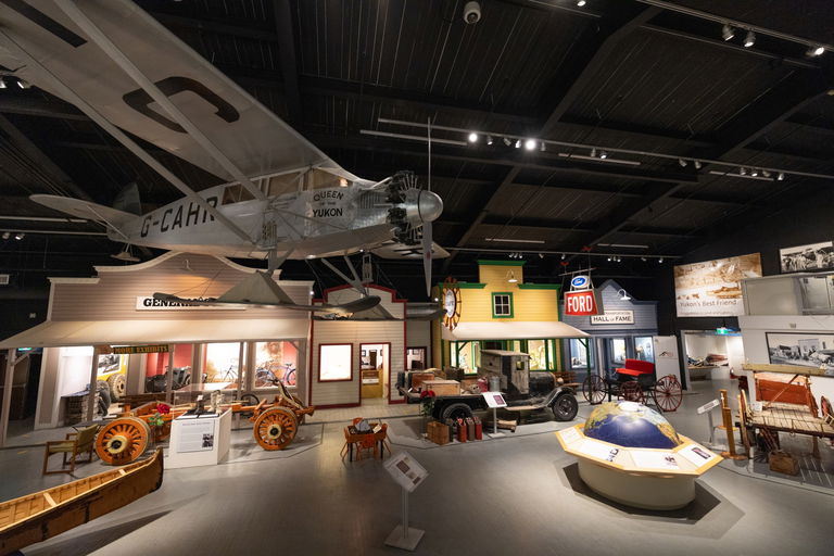 Image shows the inside of the Transportation Museums, including a plane suspended from the ceiling, two older vehicles, and four false front buildings.