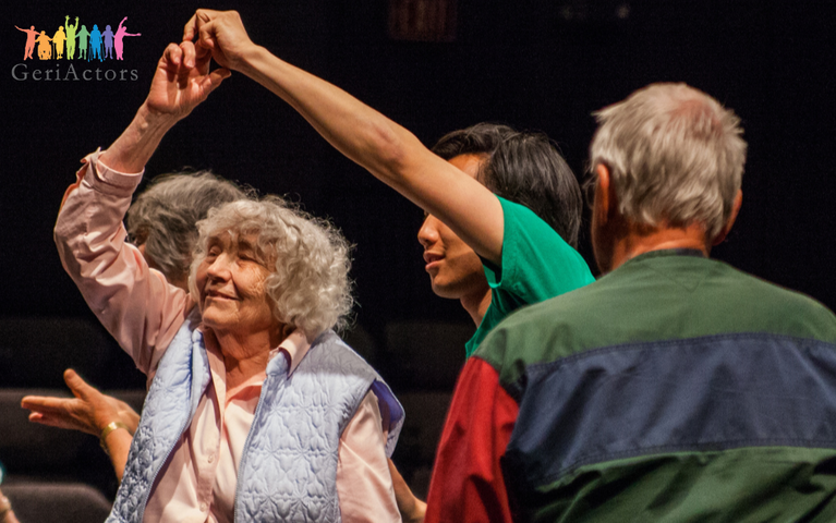An older woman and younger man are dancing on stage. Another older adult looks onto the action.