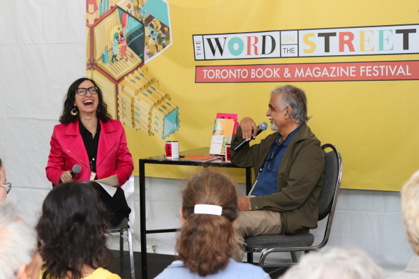 Linda Morra and M.G. Vassanji laughing while seated on stage at The Word On The Street.