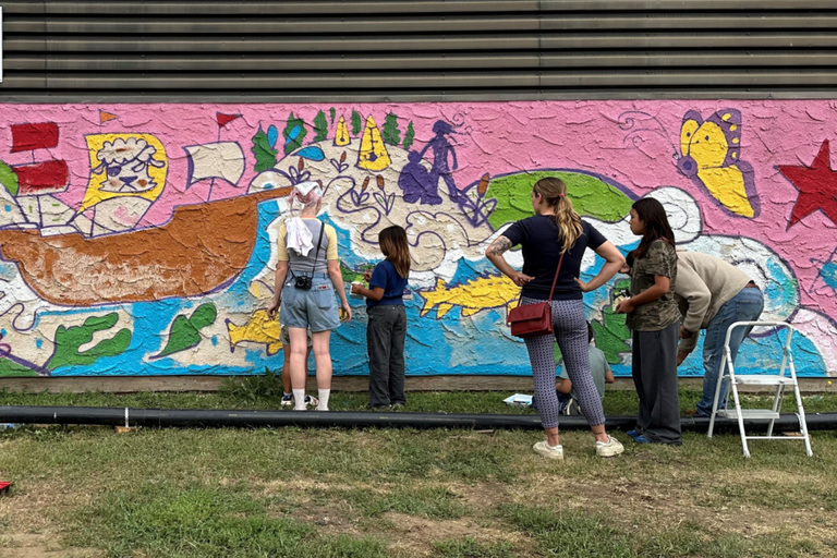 A group of community members look at and stand in front of a colourful mural