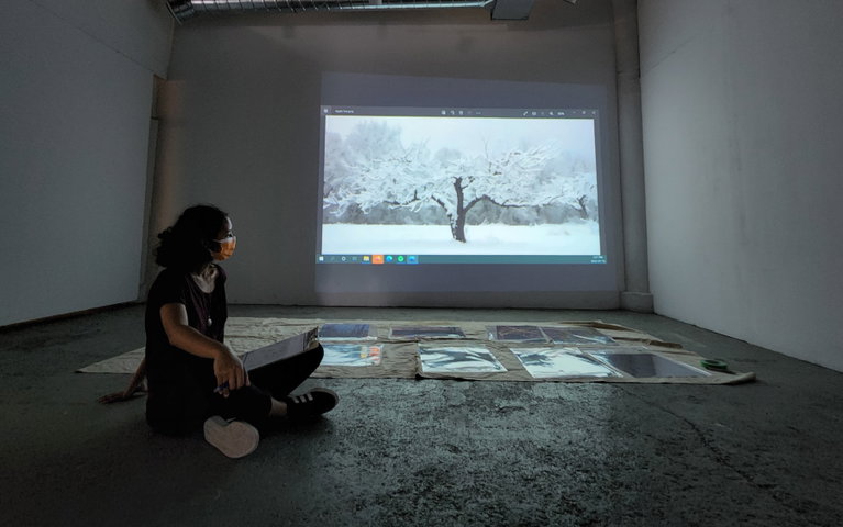 A woman sitting on the floor with a projection of a work of art behind her and several photographs laid on the ground