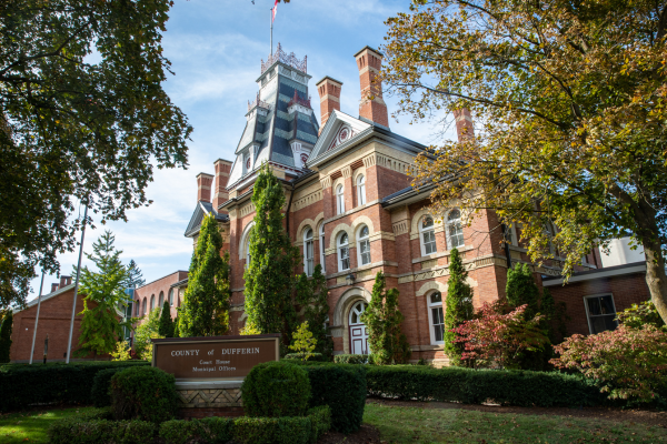 A large, ornate red and yellow brick court house with a sign in front that reads "County of Dufferin Court House and Municipal Office"