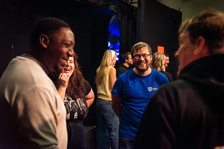 A group of performers, standing in a circle, all smiling at each other.