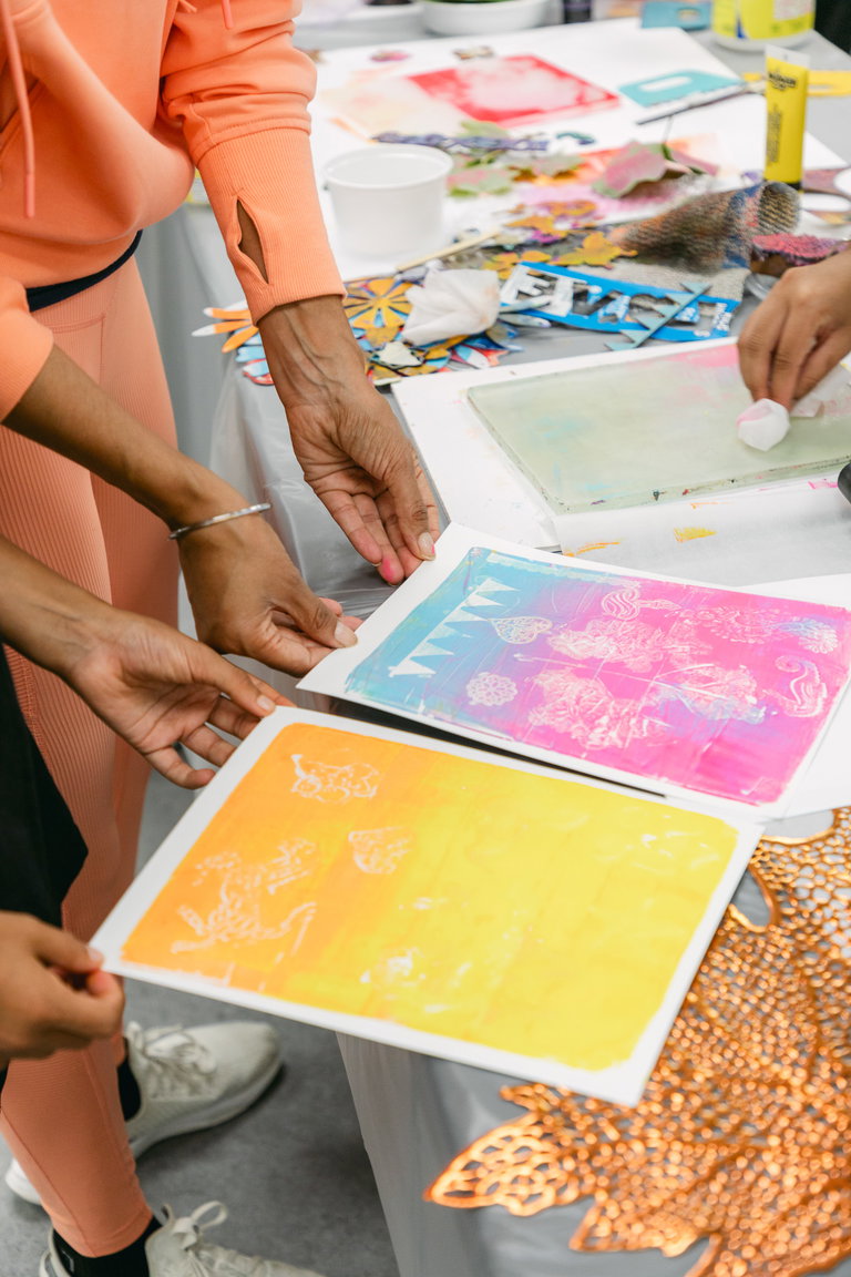 Hands holding colourful gelli prints from Taruna's workshop.