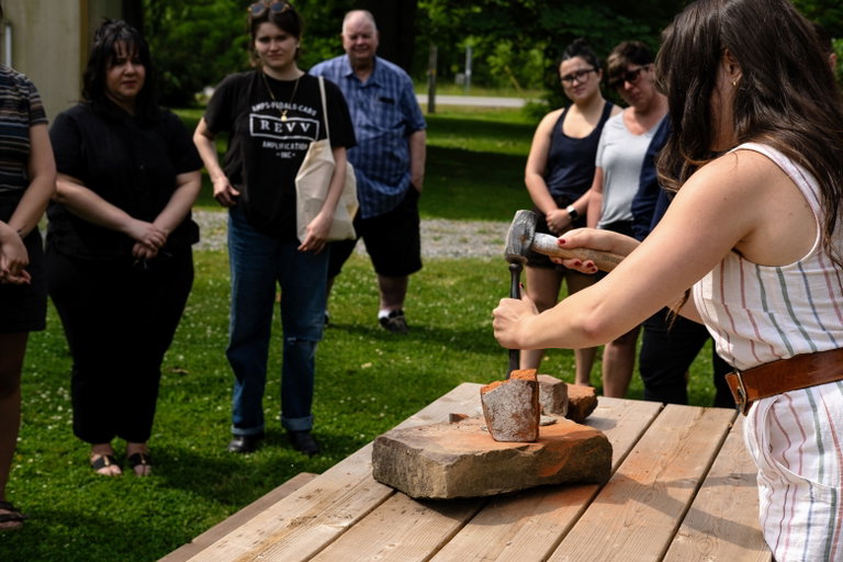 A heritage tradesperson demonstrates in front of a crowd of people. They are using a wooden mallet and chisel to collect the power of an old brick.