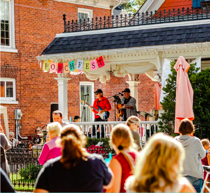 musicians playing guitars on a porch to a crowd
