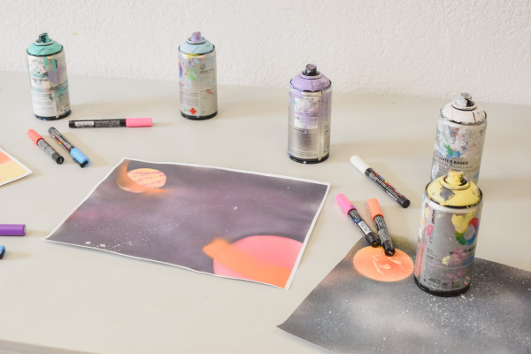 A few spray paint cans around a galaxy spray painting on a table
