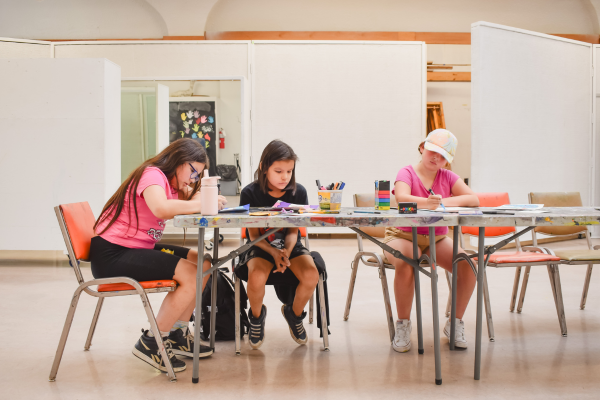 A trio of students sit around a table making art.