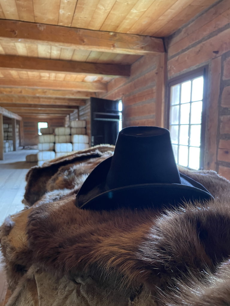 A top hat sits on a pile of fur pelts with fur packs in the background