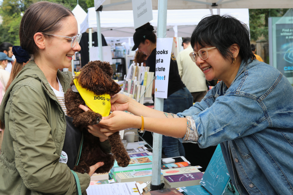 An exhibitor smiles and leans over to greet a small poodle dog visiting their tent at the festival.